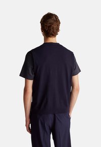 Suéter de punto sin mangas de color navy sobre una camiseta gris. La tela parece suave con una textura lisa. El diseño es simple y ajustado.
