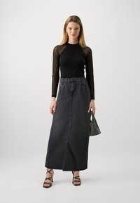 Black long-sleeve mesh top, high-waisted gray denim maxi skirt with front seam, strappy black heels, and a small black handbag.