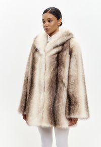 Cappotto in pelliccia sintetica color crema e marrone con ampio colletto, maniche lunghe e vestibilità ampia, caratterizzato da una superficie morbida e texturizzata.
