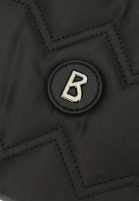 Černá prošívaná tkanina se zigzagovým švem. Obsahuje kulatou, černou gumovou nášivku se stříbrným logem "B" uprostřed.