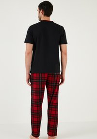 Zwarte overhemd met korte mouwen en rode kraag, gecombineerd met rode geruite broek met zwarte accenten. Comfortabele pasvorm met een casual ontwerp.