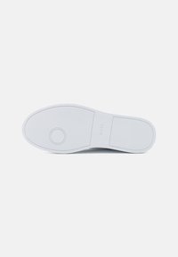 White rubber shoe sole with textured grip pattern, featuring a circular logo detail and smooth edges. Flat profile with no raised elements.