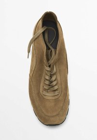 Beige mokkasiinikenkä, jossa on pyöreä kärki, paksut narut ja musta kumipohja, näkyvillä ompeluilla ja pehmustetulla sisäpohjalla.