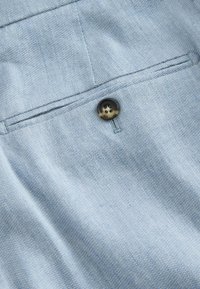 Tissu bleu clair avec une fine texture diagonale, avec un bouton rond foncé sécurisant une poche fendue étroite.