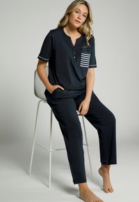 Marinblå pyjamasset med en kortärmad topp med knäppt henley-krage och randig ficka; matchande byxor, mjukt material.