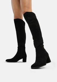 Botas de ante negras hasta la rodilla con un tacón cuadrado, que cuentan con un cierre lateral y una textura suave. Diseñadas para una silueta ajustada.