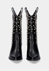 Botas de cuero negro hasta el tobillo con punteras puntiagudas y partes superiores asimétricas. Adornadas con tachuelas y estrellas plateadas para un detalle añadido.