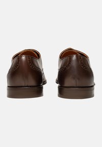 Scarpe in pelle marrone con una superficie liscia, caratterizzate da design wingtip e perforazioni decorative sul retro. Tacco basso.
