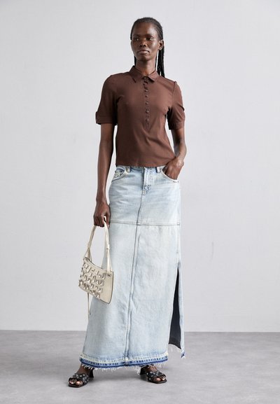 Polo shirt marron à manches courtes côtelées, jupe maxi en jean bleu clair avec fente sur le côté, sac en toile beige tissé et sandales noires à clous.