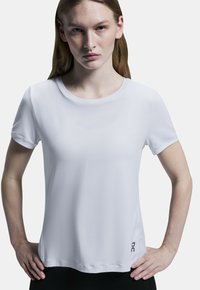 Vit kortärmad skjorta i mjukt tyg, med rundad halsringning och en liten logotyp längst ner till vänster. Designen är enkel och minimalistisk.
