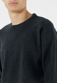 Ciemnoszary sweter dziany z okrągłym dekoltem i lekko opadającymi ramionami. Gładka faktura z subtelnymi wariacjami w materiale.