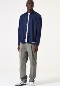 Camisa de mezclilla en azul oscuro, diseño de botones con un dobladillo curvado. Combinada con pantalones gris claro, que tienen un ajuste relajado. Zapatillas blancas con rayas negras.