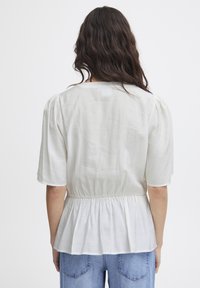 Blouse blanche à manches courtes avec taille froncée et coupe décontractée. Fabriquée en tissu léger avec une texture lisse.