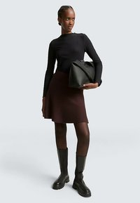 Zwarte geribbelde top met lange mouwen, wijnrode uitlopende rok, zwarte laarzen tot aan de knie en een grote zwarte handtas met een gevouwen ontwerp. Effenkleurig palet.