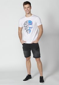 White short-sleeve t-shirt featuring a colorful graphic print of a skull and text. Paired with dark gray cargo shorts and black sneakers.