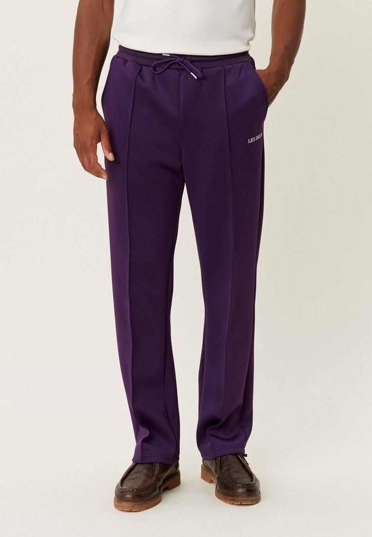 Pantalones deportivos morados ligeros con cintura ajustable con cordón, costuras laterales y un logo impreso en el muslo izquierdo. Textura suave.