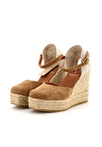Sandalo con zeppa in suede marrone, dotato di fasce in tessuto intrecciato, dettagli in corda di juta e una punta chiusa. Presenta una cinghia alla caviglia con fibbia per maggiore sicurezza.