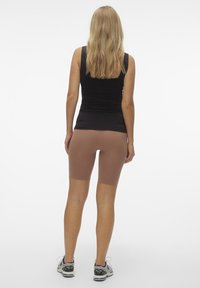 Hnědé cyklistické šortky v kombinaci s přiléhavým černým topem, který má hladkou texturu a délku do poloviny stehna. Celkový vzhled doplňují pohodlné sportovní boty.