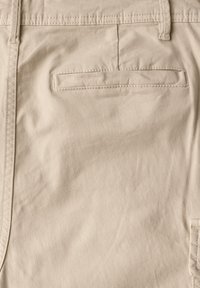 Béžová bavlněná tkanina s hladkou strukturou. Obsahuje zadní kapsu s vodorovným švem a kontrastním šitím podél okrajů.