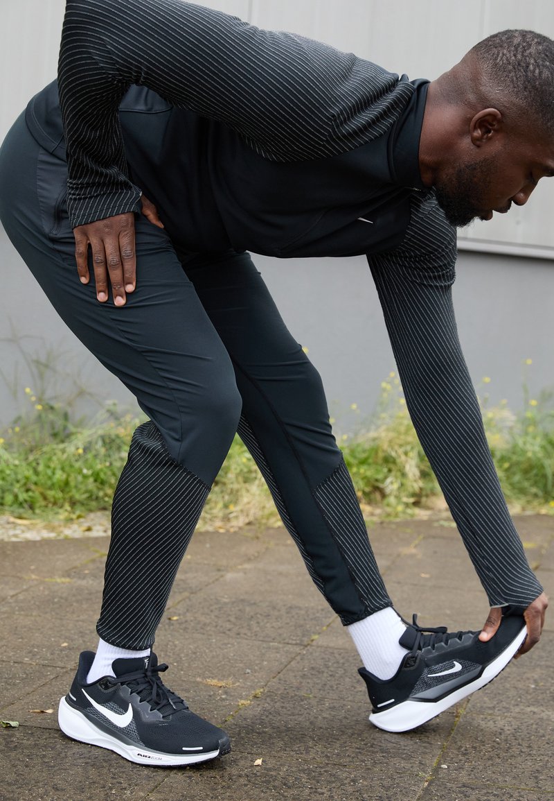 Ropa deportiva negra que incluye una camiseta larga de manga con textura de rayas y pantalones ajustados, combinados con zapatillas Nike en blanco y negro.