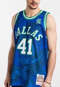 Camiseta de baloncesto azul con "DALLAS" en verde, número "41" en blanco y patrón de dragón. Cuello acanalado en verde y blanco, etiqueta en el dobladillo.