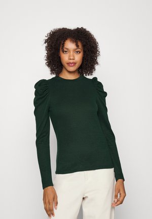 Dark green long-sleeve top with puffed shoulders, crew neckline, and a smooth texture. Worn with light-colored pants.