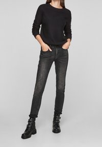 Pull en maille noir, jean gris ajusté et bottes de combat noires avec boucles. Ce look présente un design décontracté en couches.