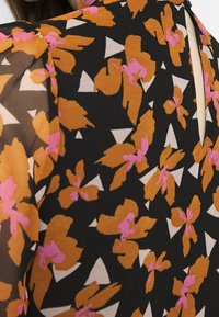 Svart tyg med stora orange blommor och rosa accenter, samt vita triangelformer. Inkluderar ett bakre nyckelhålsdetalj och texturerad design.