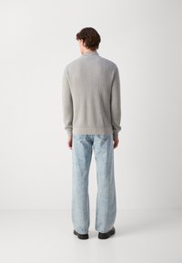 Maglione grigio a coste con maniche lunghe, abbinato a jeans a gamba larga di un blu chiaro e scarpe nere, visto da dietro.