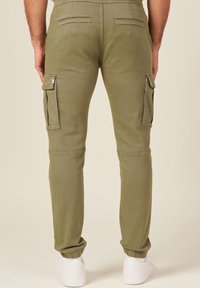 Cargo-Hosen in Olivgrün, aus Baumwollmischung. Mit elastischen Bündchen, Seitentaschen und einer glatten Textur. Eingeschnittene Gesäßtaschen.