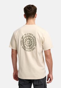 Camiseta de algodón beige con manga corta, presenta un gráfico espiral y el texto "CADA DÍA ES UN NUEVO COMIENZO" en verde oscuro en la parte posterior.