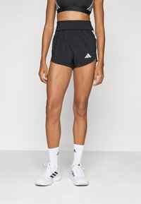 Sorte idrettsshorts med bred midje, sidelommer og det ikoniske hvite Adidas-logoet; kombinert med hvite sokker og sportsko.