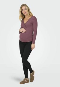 Puha bordázott anyagú kismama felső, mély V-kivágással és csipkebetéttel, fekete leggingsszel és barna sportcipővel, rózsaszín részletekkel párosítva.