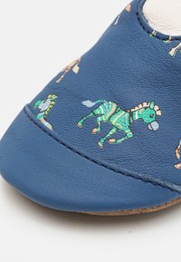Chaussure en cuir bleue avec des motifs animaliers représentant des zèbres, des girafes et d'autres dessins. Texture lisse avec des coutures contrastées et une forme arrondie.