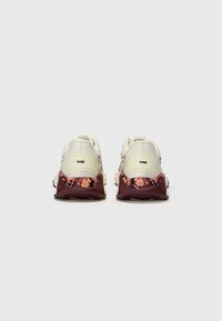 Hvite sneakers med en teksturert mellomsole som har blomstermønstre i rosa og mørkerød. Bakfra vises logodetaljer og snøring.