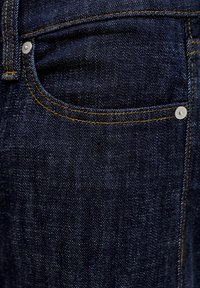 Σκούρο μπλε τζιν τζιν με χρυστά ραφές, εμπρόσθια τσέπη με μεταλλικό καρφίτσα και ομαλή υφή.