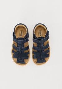 Sandalias de ante azul marino con un diseño abierto, que cuentan con correas ajustables y una suela de goma marrón. Forro interior suave.