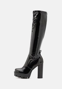 Mustat polven yli ulottuvat saappaat kiiltävällä pinnalla, paksulla alustalla ja korkealla korolla. Sisältää ommeltuja yksityiskohtia ja vetotarran takana.