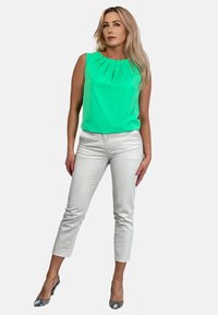 Miętowa, bezrękawnikowa bluzka z plisowanym dekoltem, zestawiona z białymi spodniami o kroju 3/4 i obcasami w wzór węża; gładki materiał, dopasowany krój.