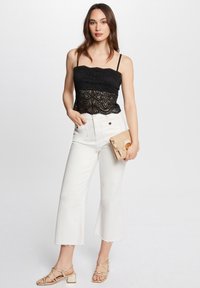 Top corto in pizzo nero con spalline sottili, jeans bianchi a vita alta con orlo sfrangiato, sandali dorati con cinturini e borsa a tracolla intrecciata.