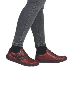 Baskets en cuir rouge avec accents noirs, présentant une fermeture éclair sur le côté, un laçage à l'avant et une semelle en caoutchouc texturée. Portées avec un jean sombre et des chaussettes.