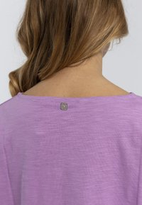 T-shirt lilla chiaro con una vestibilità rilassata. Tessuto morbido, scollo a barca e un piccolo etichetta di marca situata sul retro vicino allo scollo.