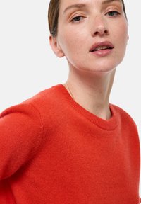 Pull rouge à col rond, fabriqué en tissu doux. Présente une texture lisse et une coupe ajustée, mettant en valeur une silhouette épurée.