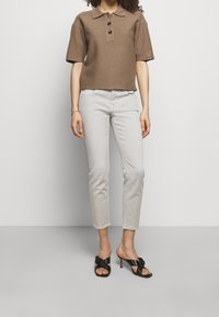 Polo marron à manches courtes avec trois boutons, jean slim gris clair, et sandales à talons noires avec un détail de nœud.