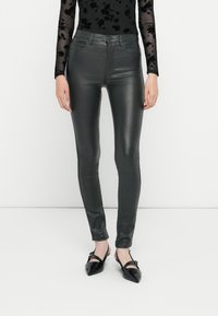 Υψηλόμεσα, μεταλλικά γκρι στενά παντελόνια με λεία, λαμπερή υφή· διαθέτουν εμπρόσθιες τσέπες και κλείσιμο με φερμουάρ.