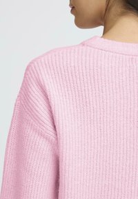 Pulover tricotat roz, cu un model texturat în relief și un guler larg rotund, cu o croială relaxată și cusături de umeri căzute.