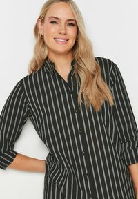 Camicia a maniche lunghe a righe nere e grigie, con colletto ripiegato e taschino sul petto; tessuto liscio con una leggera lucentezza.