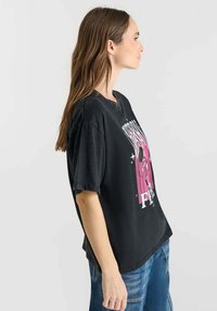 Camiseta negra de gran tamaño con un diseño gráfico en rosa que presenta estrellas y texto, hecha de tela de algodón, con un ajuste relajado y cuello redondo.