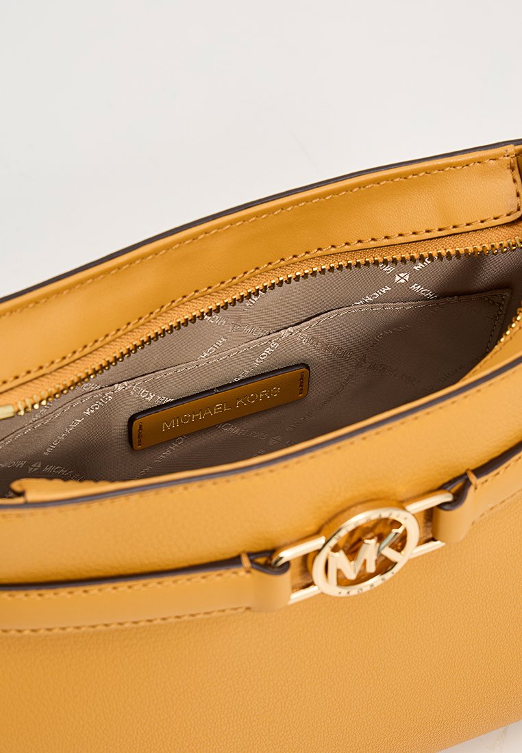 Geel leren handtas met een gladde textuur, gouden hardware en een ritssluiting. Binnenin heeft het een voering met logo en een klein label.