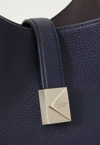 Navy leather handbag with a textured surface, featuring a gold triangular hardware detail and a sturdy handle.